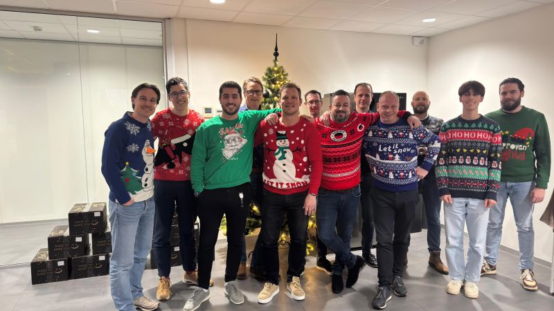 Het team van Vintus in foute kersttruien op kantoor, naast de kerstboom